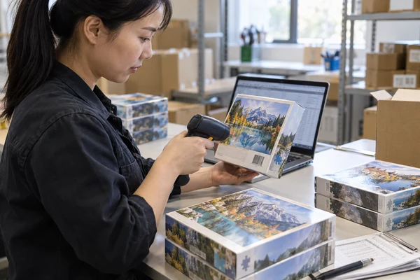 Asian adult inspector scanning a plain retail puzzle box at a packing bench