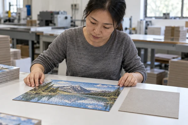 Asian adult quality inspector examining a flat thin cardboard puzzle beside a greyboard sheet