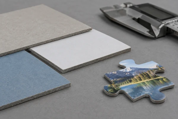 Thin grey and blue-core cardboard samples and a printed puzzle piece beside a closed caliper