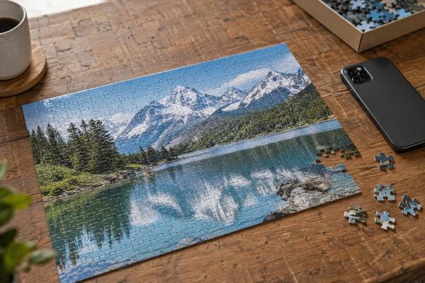 mountain travel photograph printed as a cardboard puzzle beside a smartphone face down