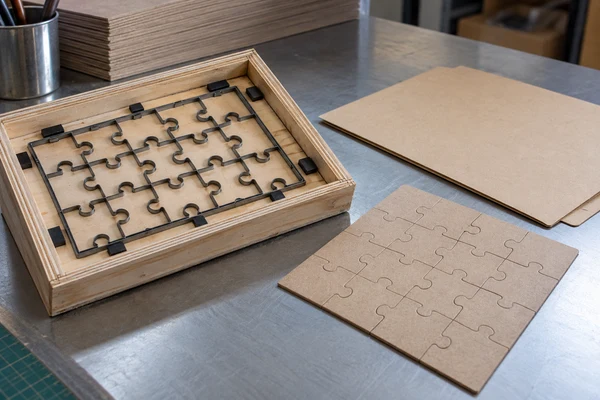 Protected steel-rule puzzle die beside cardboard prototype sheets